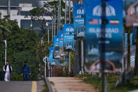 People walk past a row of billboards of the US-Iran talks.